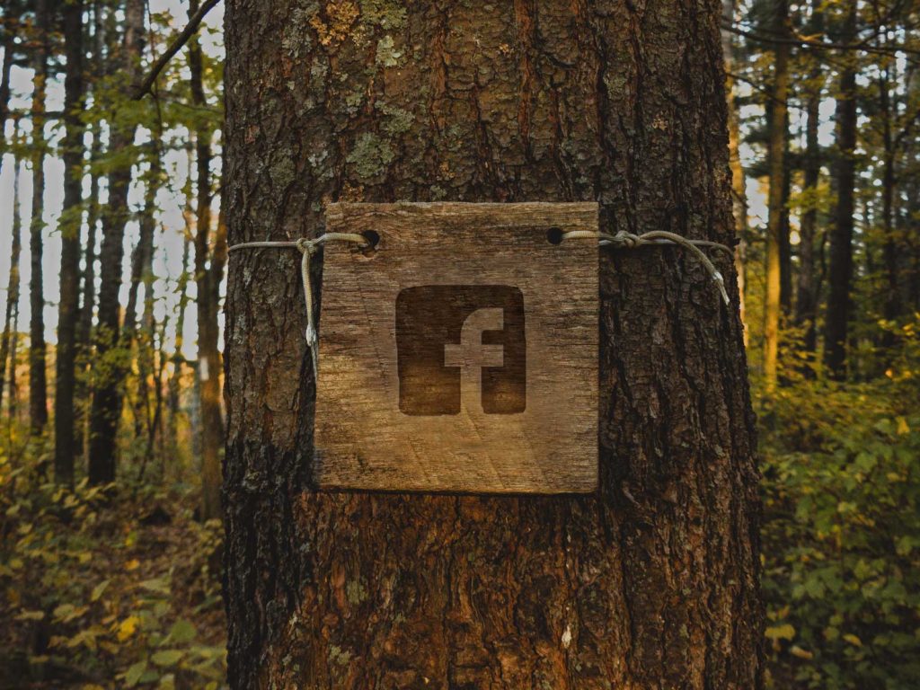 A wooden placard with the Facebook logo is tied around a tree. 