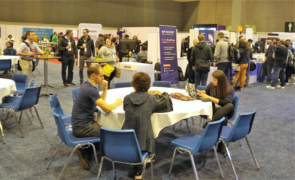 A crowd of WordCamp US attendees network and discuss WordPress. 