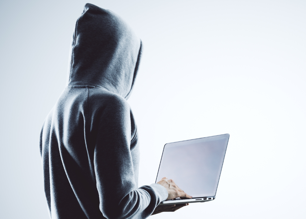 A man in a hoodie holds a laptop computer. 